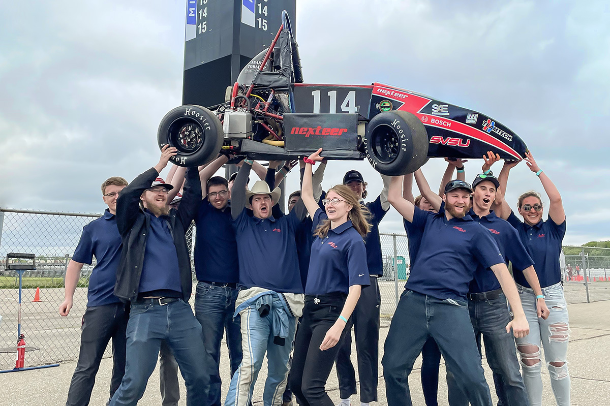 group of young people raising a small race car overhead